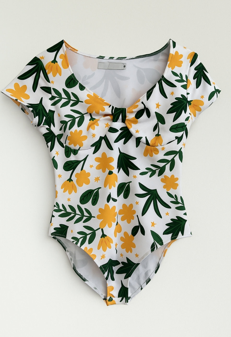 Body de mujer de manga corta, escote en V y detalle en pecho, con cazuelas y estampado con flores amarillas. Tela de lycra elástica